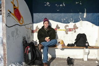 Chad at the bus stop eating a sandwich waiting for the last bus of the day.